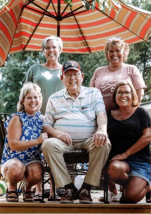 Ray Teaster seated with his family on a deck under a striped umbrella